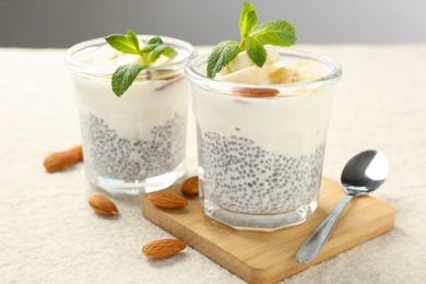 Photo of Delicious dessert with chia seeds, yogurt, banana, almond and mint in glasses on light textured table, closeup. Superfood