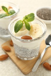Photo of Delicious dessert with chia seeds, yogurt, banana, almond and mint in glasses on light table, closeup. Superfood