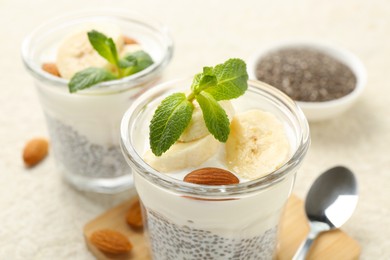 Photo of Delicious dessert with chia seeds, yogurt, banana, almond and mint in glasses on light table, closeup. Superfood