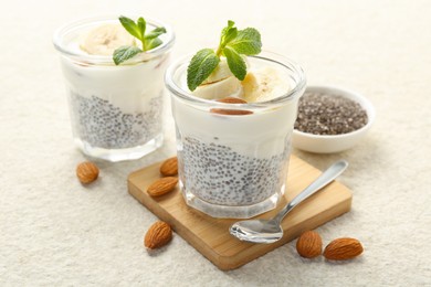 Photo of Delicious dessert with chia seeds, yogurt, banana, almond and mint in glasses on light textured table, closeup. Superfood