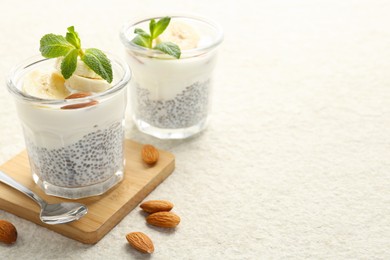 Photo of Delicious dessert with chia seeds, yogurt, banana, almond and mint in glasses on light textured table, closeup with space for text. Superfood