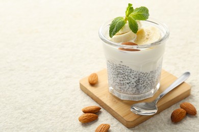 Photo of Delicious dessert with chia seeds, yogurt, banana, almond and mint in glass on light textured table, closeup with space for text. Superfood