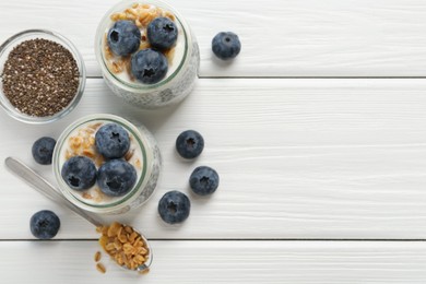 Photo of Delicious pudding with chia seeds, yogurt, blueberries and granola on white wooden table, flat lay with space for text. Superfood