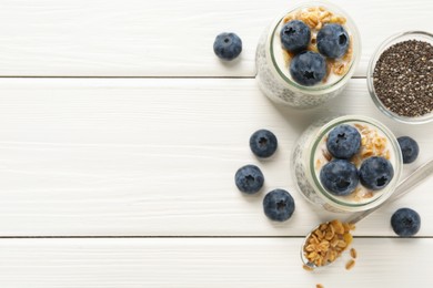 Photo of Delicious pudding with chia seeds, yogurt, blueberries and granola on white wooden table, flat lay with space for text. Superfood