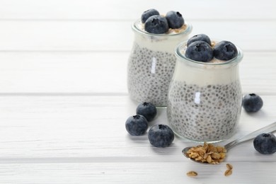 Photo of Delicious pudding with chia seeds, yogurt, blueberries and granola on white wooden table, closeup with space for text. Superfood
