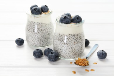 Photo of Delicious pudding with chia seeds, yogurt, blueberries and granola on white wooden table, closeup. Superfood