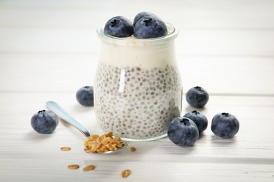 Photo of Delicious pudding with chia seeds, yogurt, blueberries and granola on white wooden table, closeup. Superfood