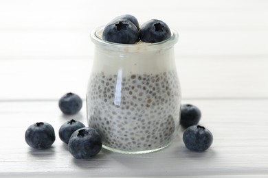 Photo of Delicious pudding with chia seeds, yogurt and blueberries in glass on white wooden table, closeup. Superfood