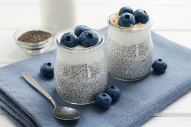 Photo of Delicious pudding with chia seeds, yogurt, blueberries and granola in glasses on white wooden table, closeup. Superfood