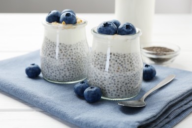 Photo of Delicious pudding with chia seeds, yogurt, blueberries and granola in glasses on white wooden table, closeup. Superfood