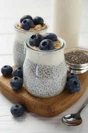 Photo of Delicious pudding with chia seeds, yogurt, blueberries and granola in glasses on white wooden table, closeup. Superfood