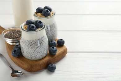 Photo of Delicious pudding with chia seeds, yogurt, blueberries and granola in glasses on white wooden table, closeup with space for text. Superfood