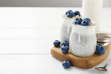 Photo of Delicious pudding with chia seeds, yogurt, blueberries and granola in glasses on white wooden table, closeup with space for text. Superfood