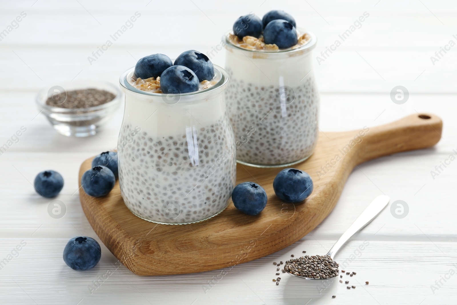 Photo of Delicious pudding with chia seeds, yogurt, blueberries and granola in glasses on white wooden table, closeup. Superfood