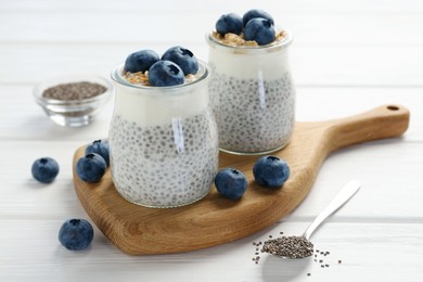 Photo of Delicious pudding with chia seeds, yogurt, blueberries and granola in glasses on white wooden table, closeup. Superfood