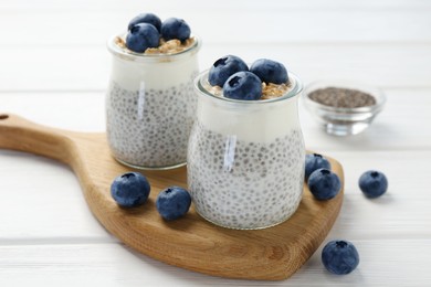 Photo of Delicious pudding with chia seeds, yogurt, blueberries and granola in glasses on white wooden table, closeup. Superfood