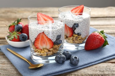Photo of Delicious dessert with chia seeds, yogurt, granola, strawberries and blueberries on wooden table, closeup. Superfood