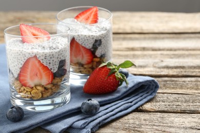 Photo of Delicious dessert with chia seeds, yogurt, granola, strawberries and blueberries on wooden table, closeup with space for text. Superfood