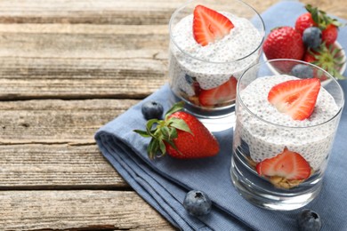 Photo of Delicious dessert with chia seeds, yogurt, strawberries and blueberries on wooden table, closeup with space for text. Superfood