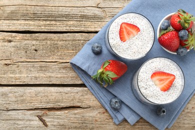Photo of Delicious dessert with chia seeds, yogurt, strawberries and blueberries on wooden table, top view with space for text. Superfood