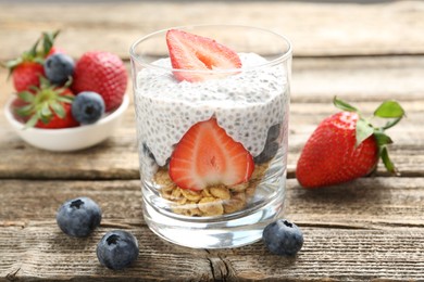 Photo of Delicious dessert with chia seeds, yogurt, granola, strawberries and blueberries in glass on wooden table, closeup. Superfood