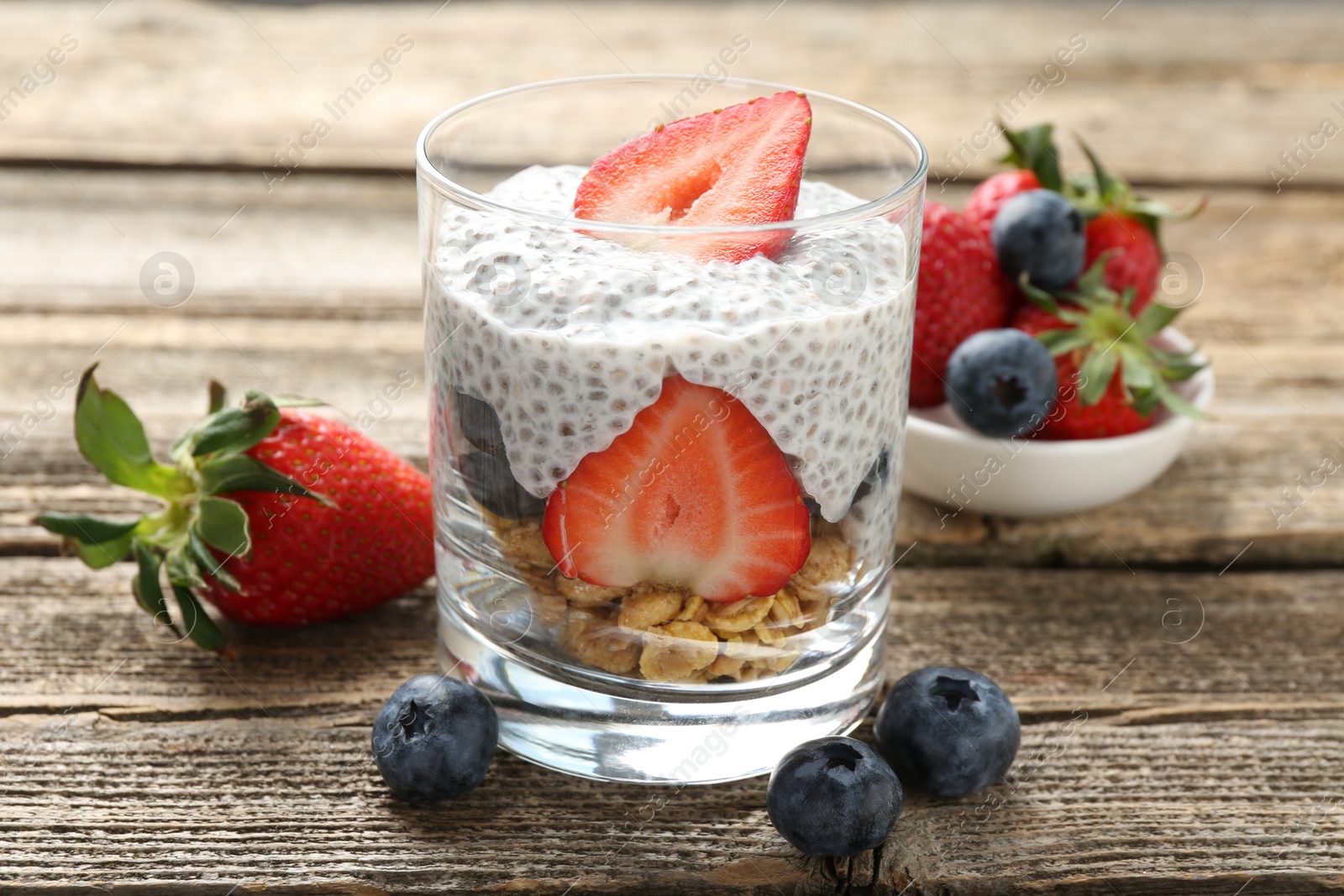 Delicious dessert with chia seeds, yogurt, granola, strawberries and blueberries in glass on wooden table, closeup. Superfood Photo of Delicious dessert with chia seeds, yogurt, granola, strawberries and blueberries in glass on wooden table, closeup. Superfood
