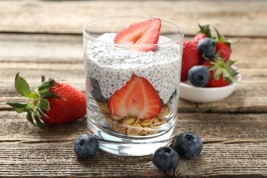 Photo of Delicious dessert with chia seeds, yogurt, granola, strawberries and blueberries in glass on wooden table, closeup. Superfood