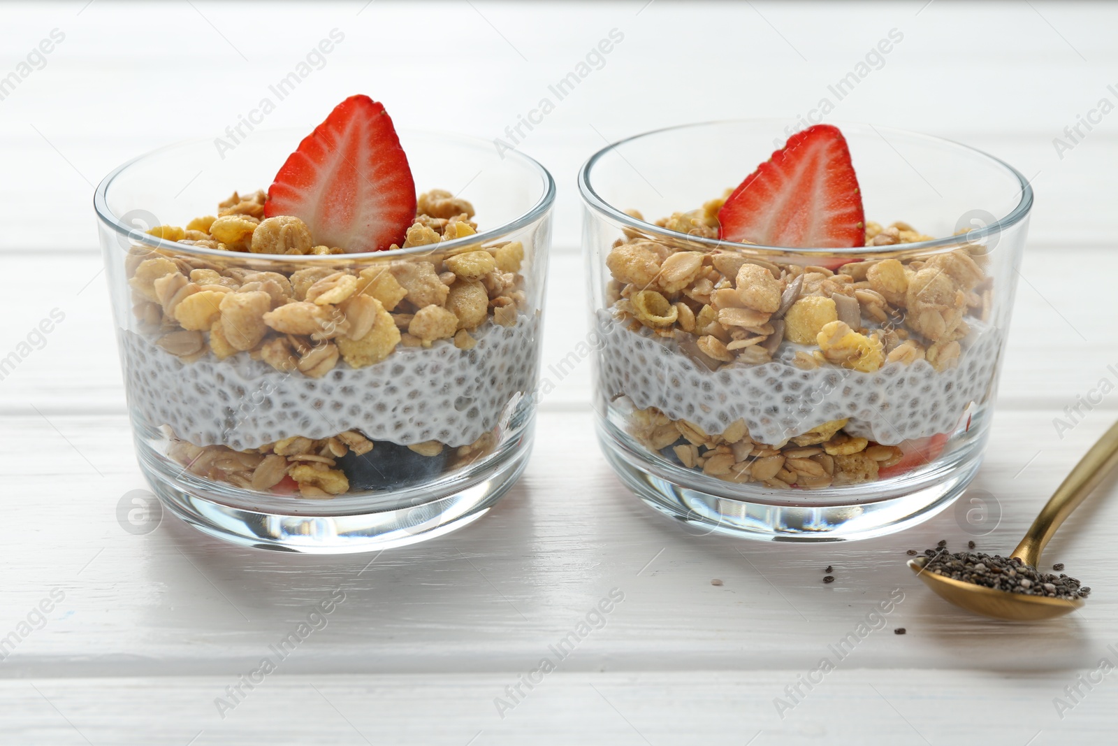 Photo of Delicious dessert with chia seeds, yogurt, granola and strawberries in glasses on white wooden table, closeup. Superfood