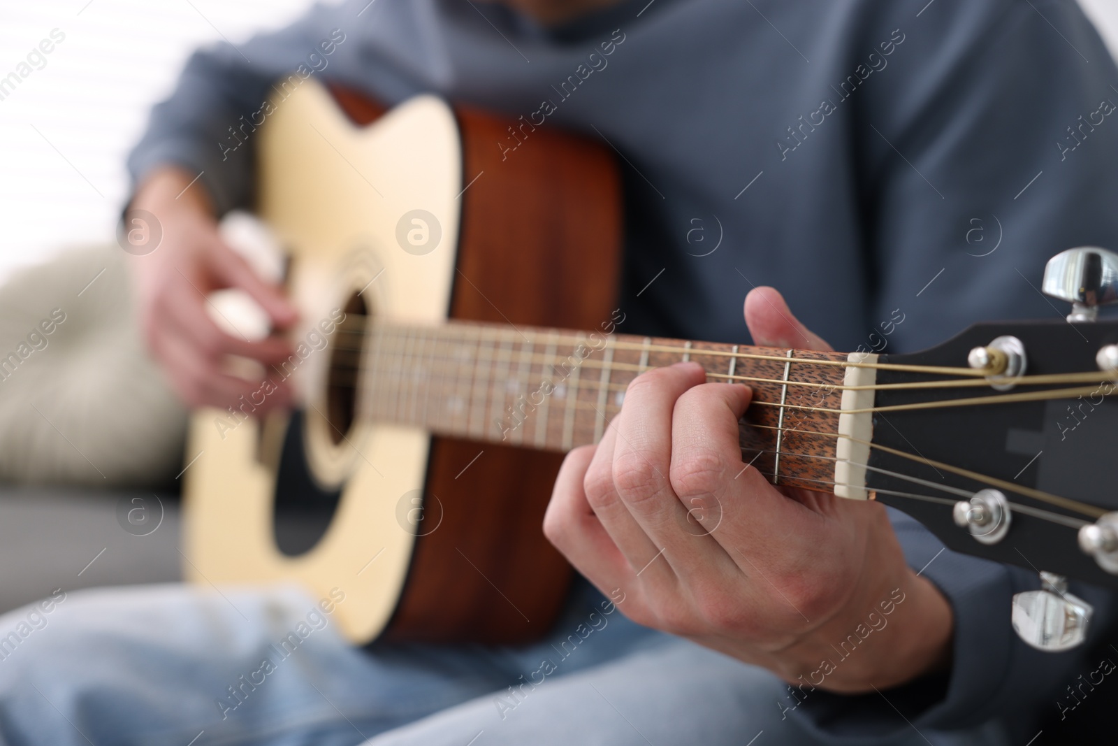 Young man playing guitar on sofa indoors, closeup Photo of Young man playing guitar on sofa indoors, closeup