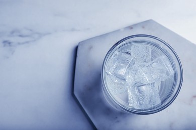 Image of Glass of soda water with ice on white marble table, top view. Space for text