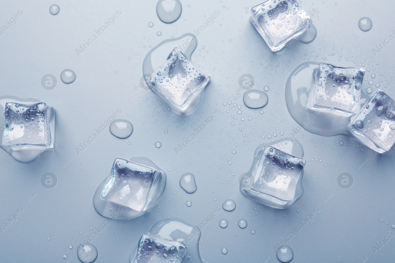 Melting ice cubes and water drops on light blue background, flat lay Image of Melting ice cubes and water drops on light blue background, flat lay