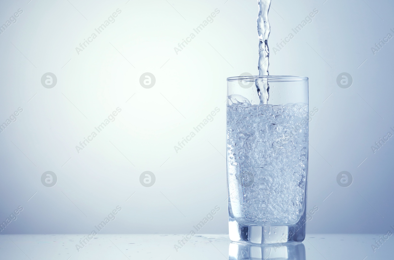 Pouring refreshing soda water into glass on light blue background, closeup. Space for text Image of Pouring refreshing soda water into glass on light blue background, closeup. Space for text