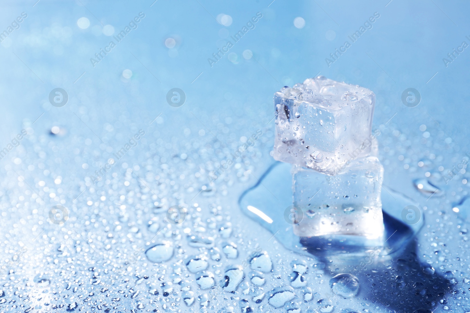 Melting ice cubes and water drops on light blue background, closeup. Space for text Image of Melting ice cubes and water drops on light blue background, closeup. Space for text