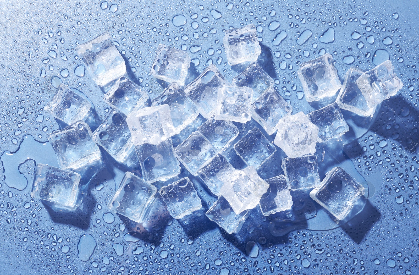 Melting ice cubes and water drops on blue background, flat lay Image of Melting ice cubes and water drops on blue background, flat lay