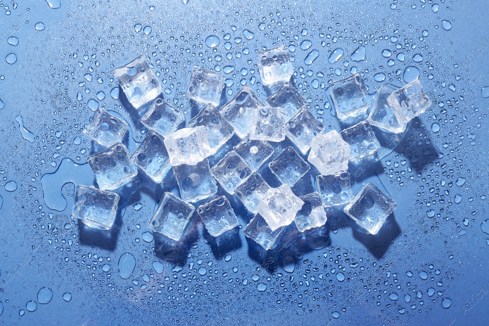 Melting ice cubes and water drops on blue background, flat lay Image of Melting ice cubes and water drops on blue background, flat lay
