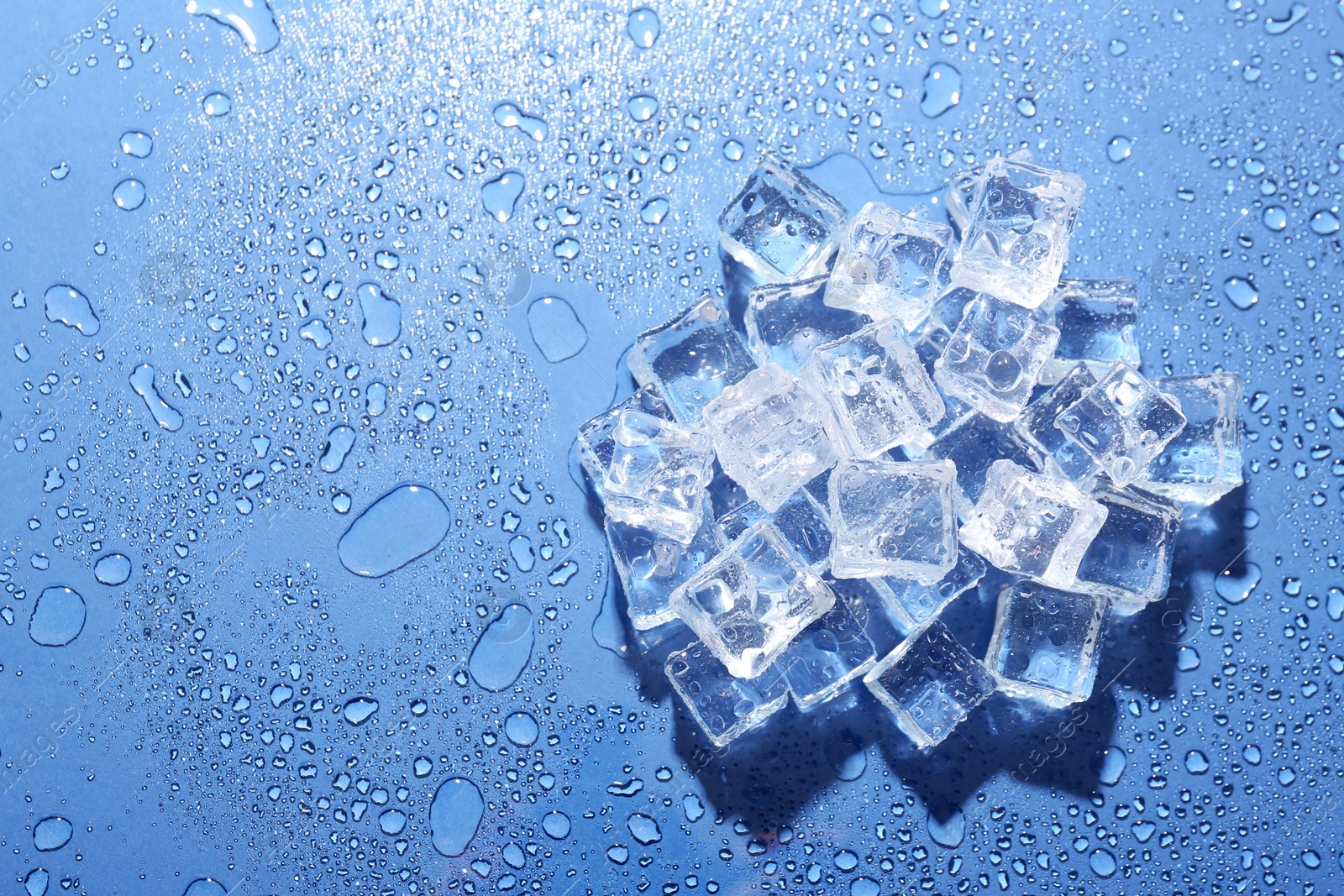 Pile of melting ice cubes and water drops on blue background, top view. Space for text Image of Pile of melting ice cubes and water drops on blue background, top view. Space for text