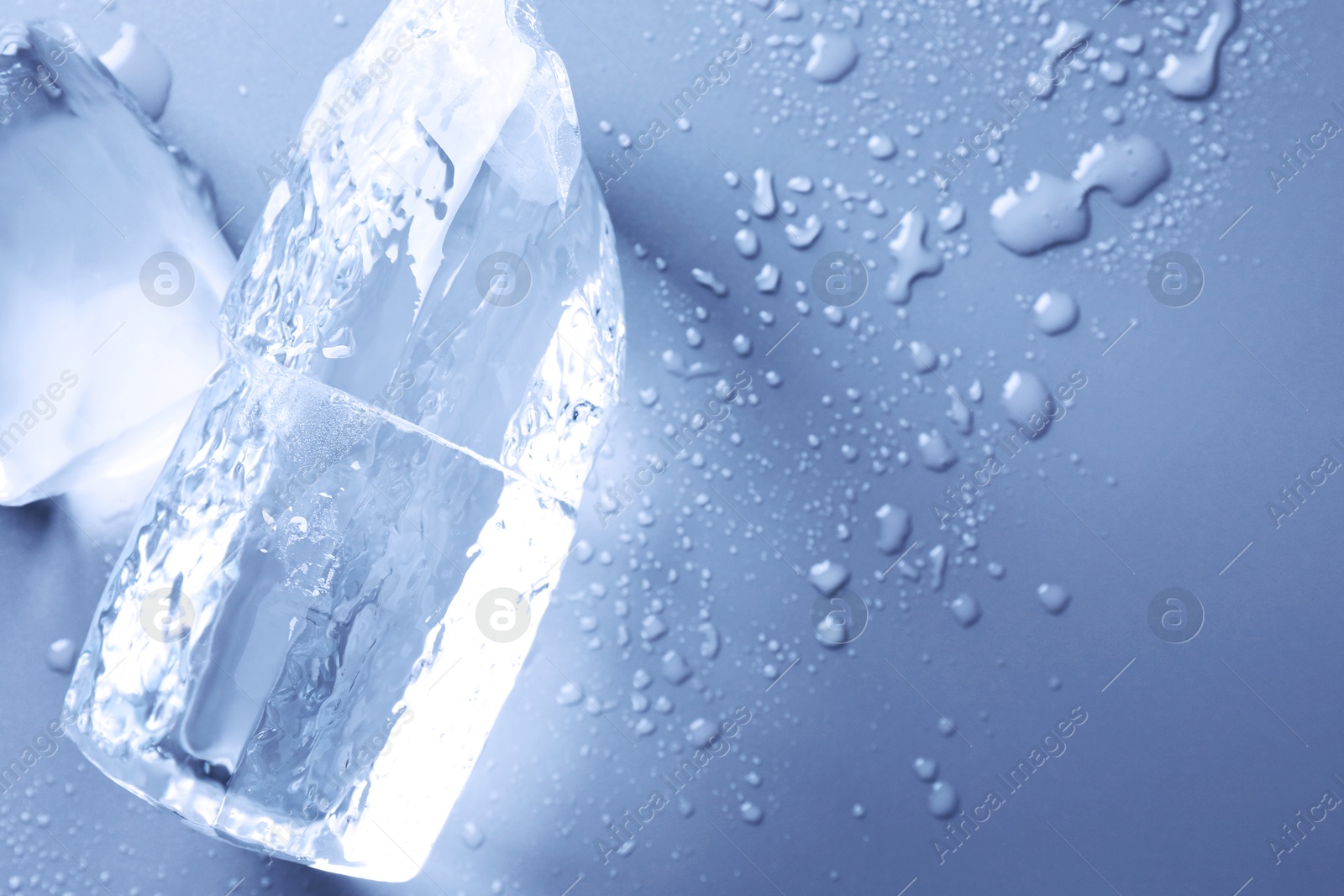 Pieces of clear ice and water drops on light blue table, top view. Space for text Image of Pieces of clear ice and water drops on light blue table, top view. Space for text