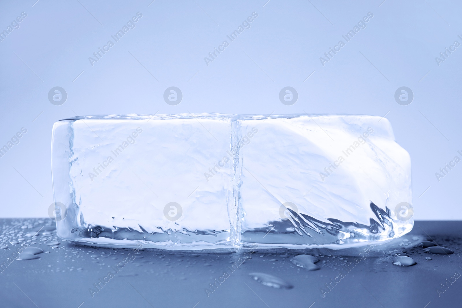Piece of clear ice and water drops on light blue table Image of Piece of clear ice and water drops on light blue table