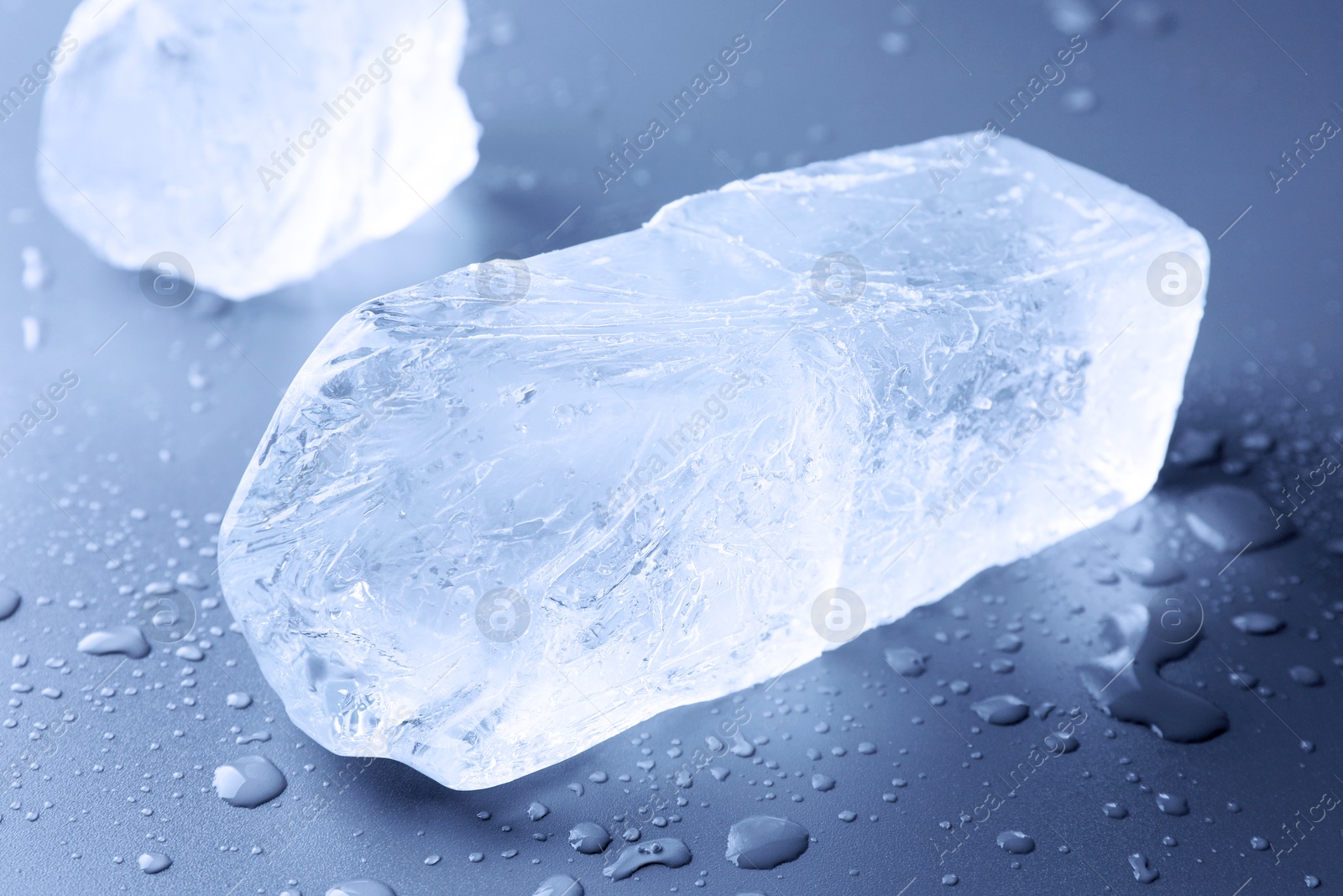 Pieces of clear ice and water drops on light blue table, closeup Image of Pieces of clear ice and water drops on light blue table, closeup