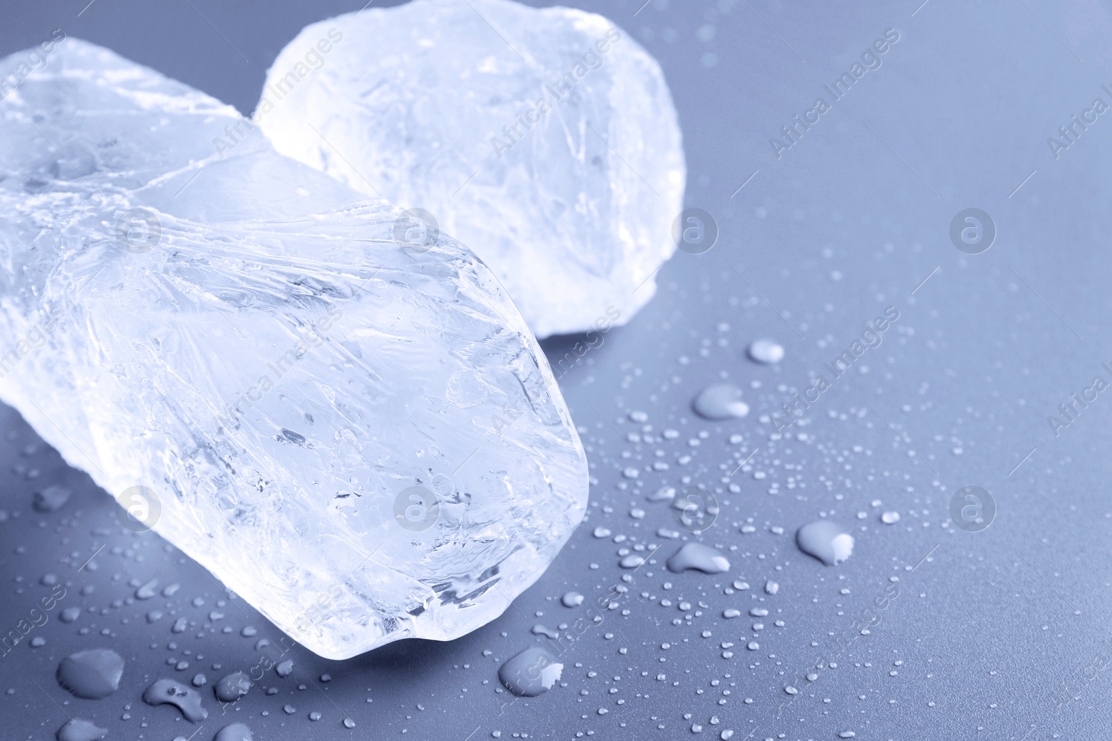 Pieces of clear ice and water drops on light blue table, closeup. Space for text Image of Pieces of clear ice and water drops on light blue table, closeup. Space for text