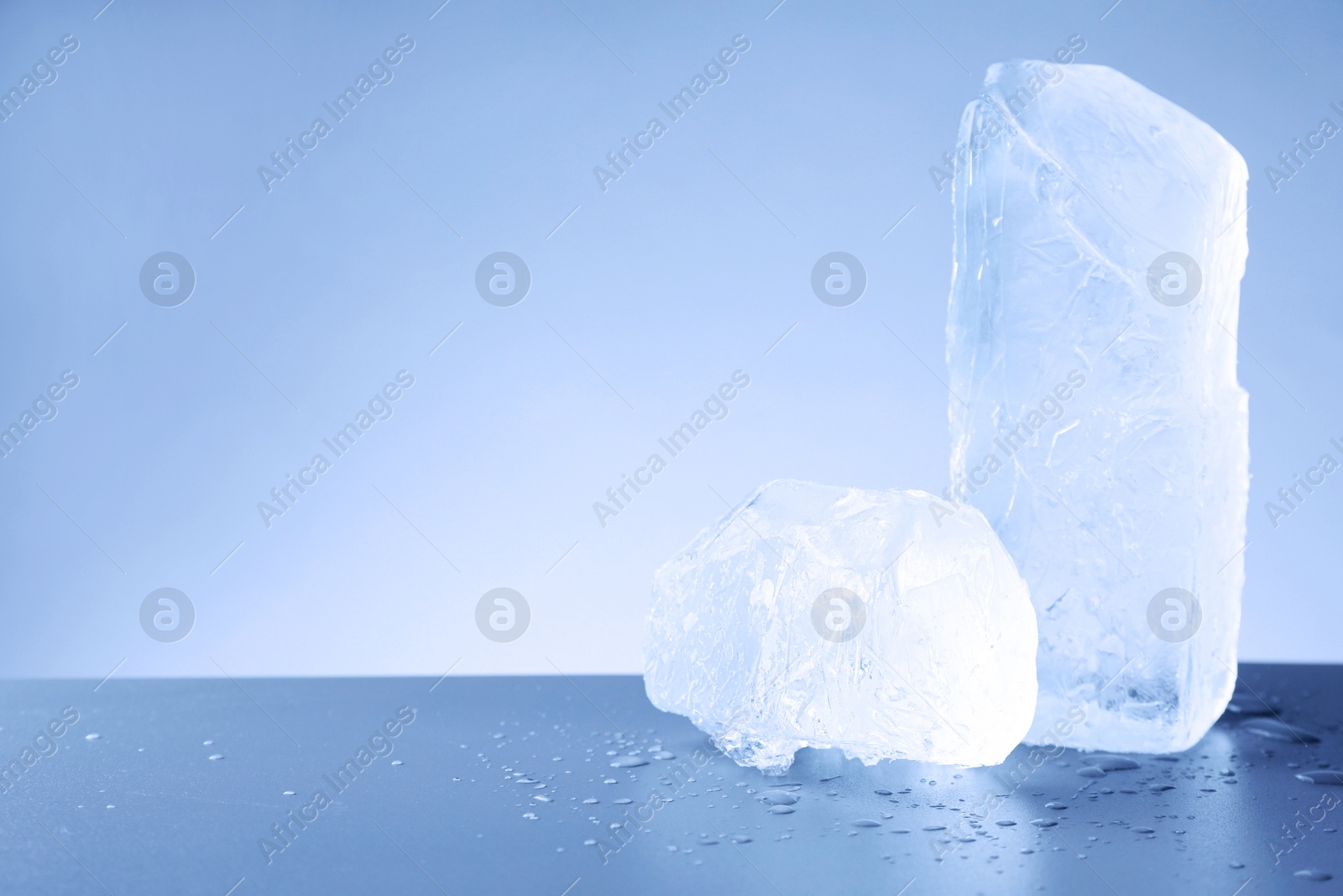 Pieces of clear ice and water drops on light blue table. Space for text Image of Pieces of clear ice and water drops on light blue table. Space for text
