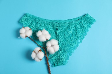 Photo of Women's underwear. Beautiful turquoise panties and cotton flowers on light blue background, top view