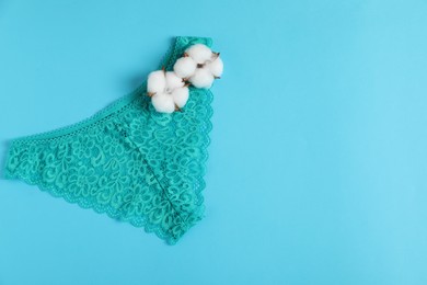 Photo of Women's underwear. Beautiful turquoise panties and cotton flowers on light blue background, top view. Space for text