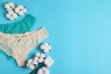 Photo of Women's underwear. Beautiful panties and cotton flowers on light blue background, flat lay. Space for text