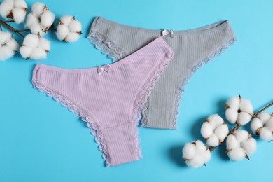 Photo of Women's underwear. Beautiful panties and cotton flowers on light blue background, flat lay