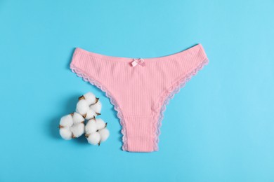 Photo of Women's underwear. Beautiful pink panties and cotton flowers on light blue background, top view