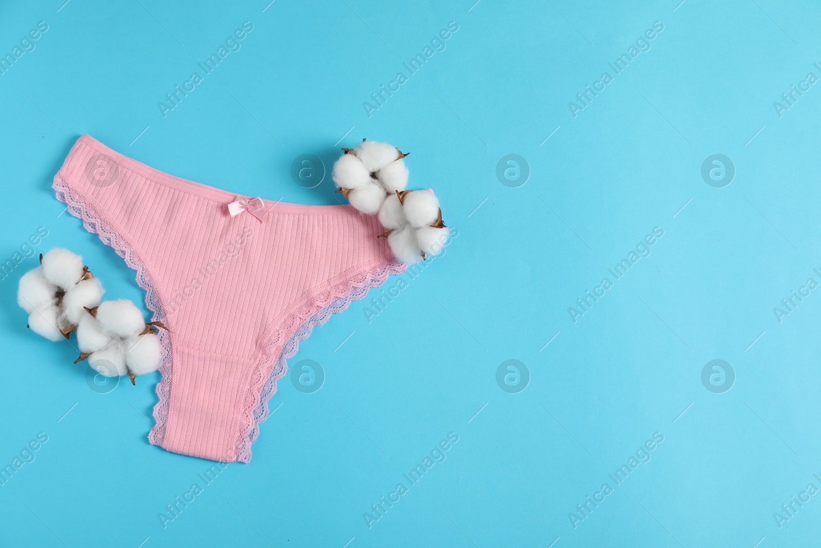 Women's underwear. Beautiful pink panties and cotton flowers on light blue background, top view. Space for text Photo of Women's underwear. Beautiful pink panties and cotton flowers on light blue background, top view. Space for text