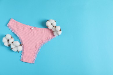 Photo of Women's underwear. Beautiful pink panties and cotton flowers on light blue background, top view. Space for text