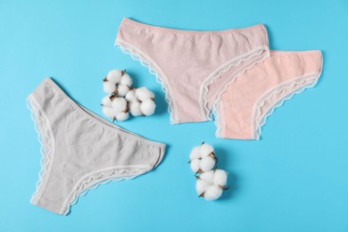 Photo of Women's underwear. Beautiful panties and cotton flowers on light blue background, flat lay
