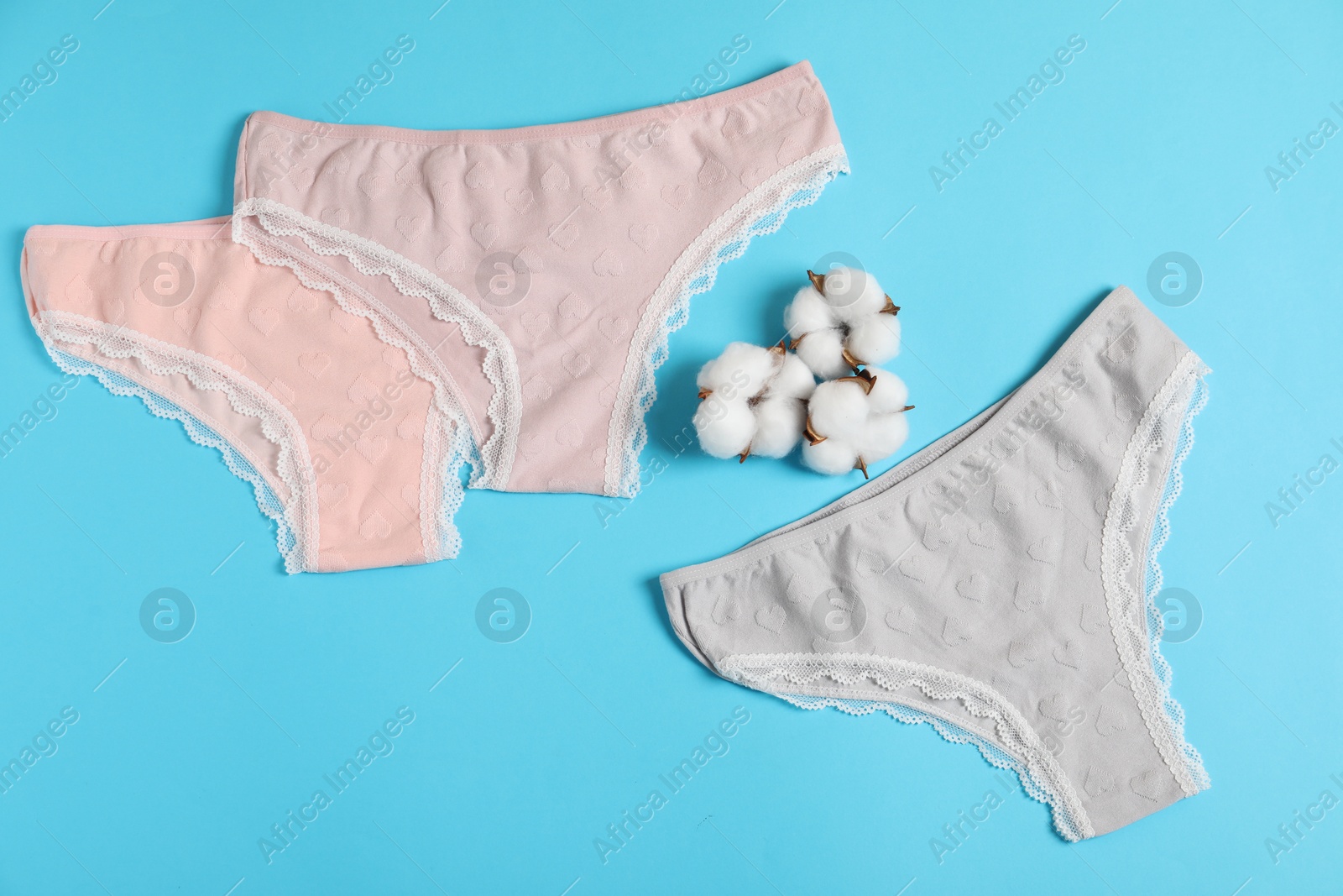Women's underwear. Beautiful panties and cotton flowers on light blue background, flat lay Photo of Women's underwear. Beautiful panties and cotton flowers on light blue background, flat lay